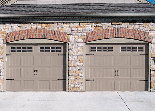 A couple of tan garage doors on a brick wall.